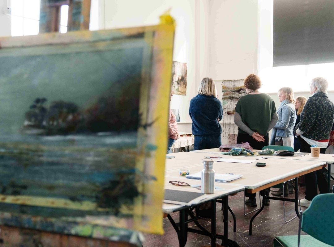 Group discussion A group of artists in a studio, deep in discussion. An unfinished landscape painting is in the foreground.